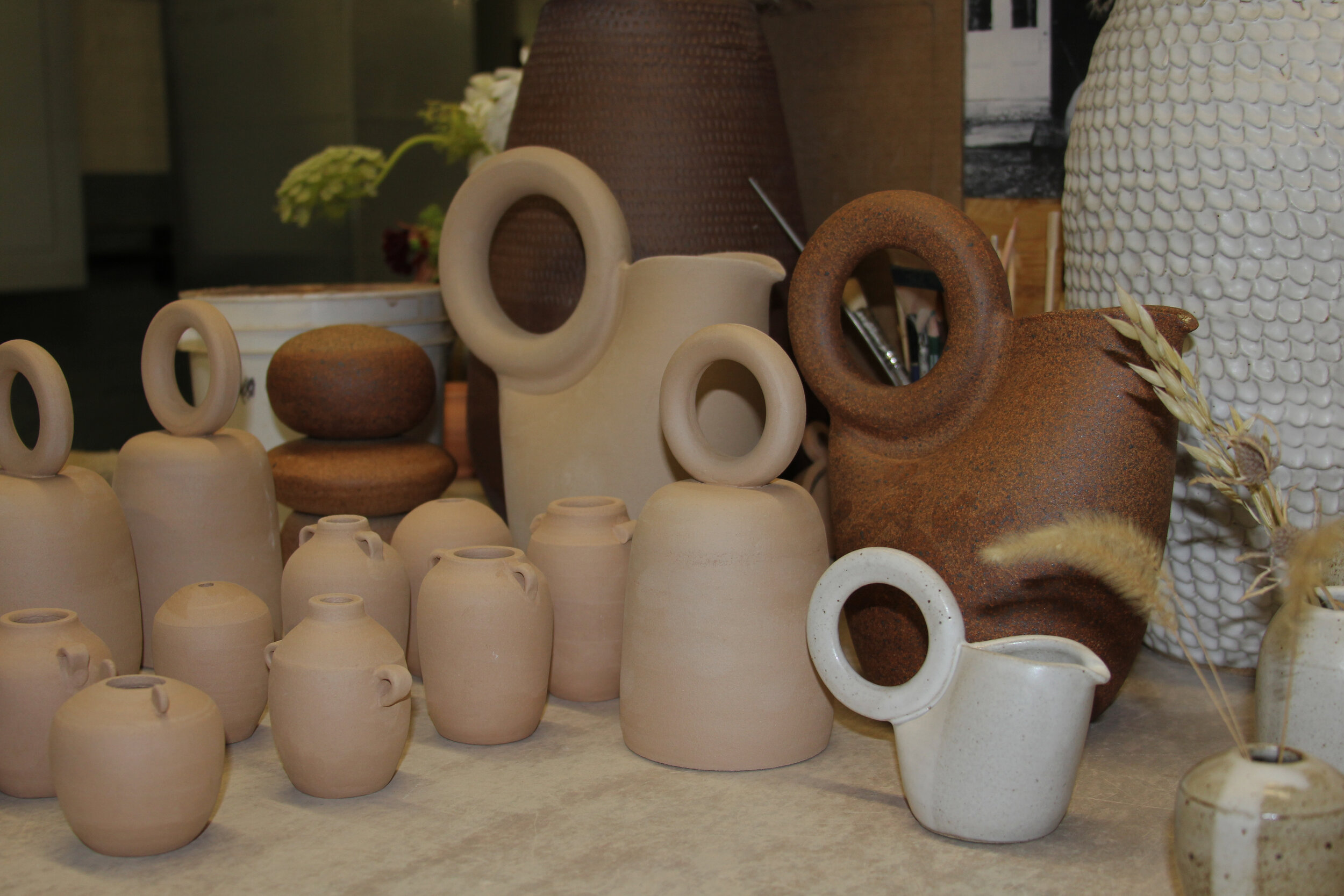Katherine recently posted the Ring Pitcher on Instagram, and the response was so good that she has started exploring doing a family with the ring in different scales. Pictured here is mostly unglazed and unfired work including: a clay cairn, Ring Pitchers both raw and fired, a small, glazed Ring Pitcher, large Ring Bells, and a handful of tiny vases.